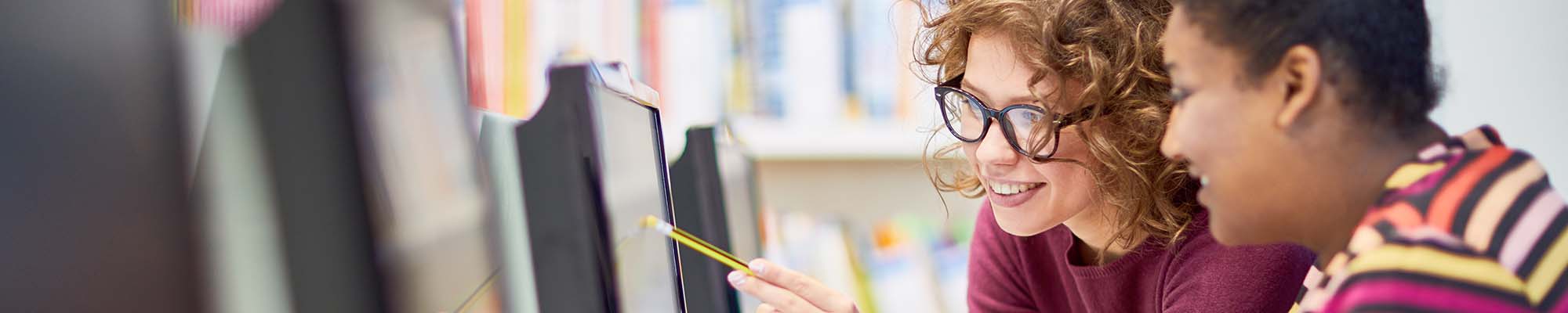 Two women look at computer, one points at screen with a pencil