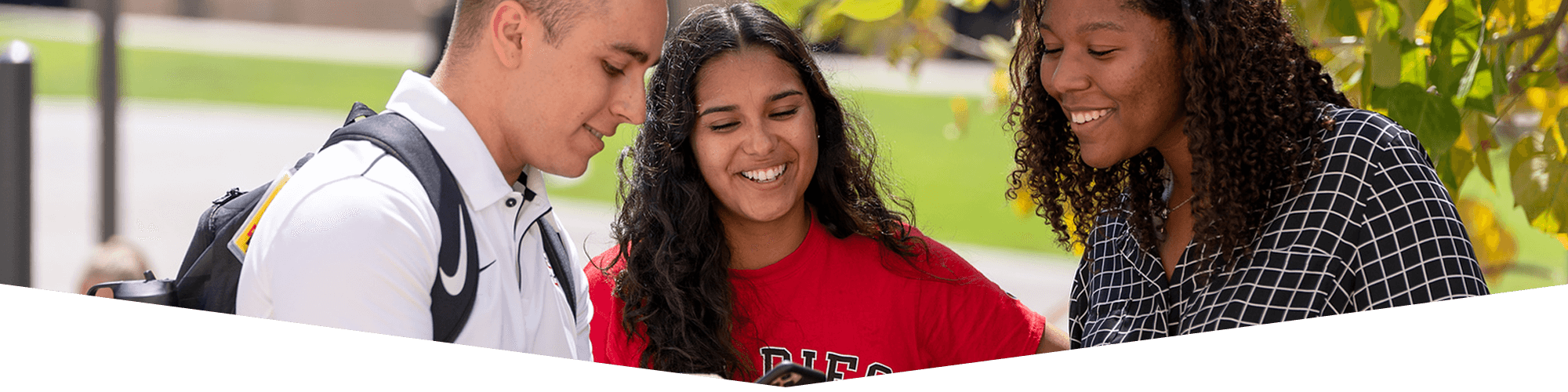 three students smiling and looking down at something